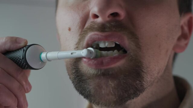 Theme of brushing and whitening teeth with a modern electric toothbrush. Close-up of a man cleaning his teeth with an ultrasonic dental brush. Morning routine, oral hygiene. Oscillating toothbrush. 
