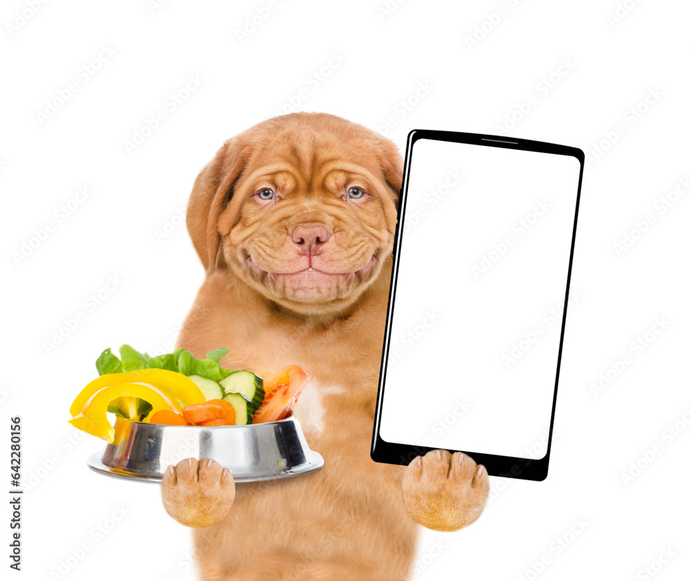 Poster Smiling puppy holding bowl of vegetables and shows empty screen of smartphone. isolated on white background