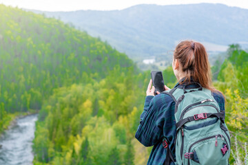 Young woman uses the smartphone at sunny mountains and using travel app or map during her hike....