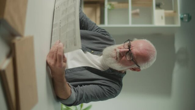 Vertical View.A Serious, Smart Old Man Sits at a Table and Reads a Newspaper.An Elderly Man with a Newspaper Alone at Home, Sees the News and Current Events in the Newspaper.Daily Newspaper Concept.