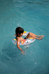 Happy Indian boy swimming in a pool, Kid wearing swimming costume along with air tube during hot summer vacations, Children boy in big swimming pool.