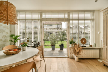 a living room with wood flooring and white shutters on the windows looking out onto an open patio...