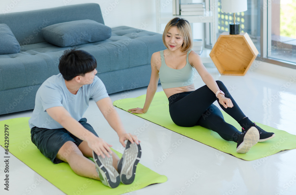 Wall mural Asian young fit male female husband and wife in sportswear sport bra legging sneakers sitting smiling on yoga mat floor stretching body exercising training practicing together in living room at home