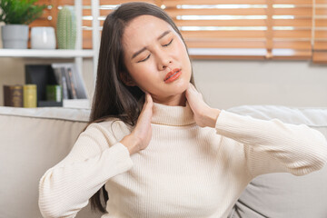 Body muscles stiff problem, asian young attractive woman, girl pain with neck pain ache from work, holding massaging rubbing shoulder hurt or sore, painful sitting on sofa at home. Healthcare people.