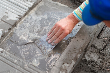 Bricklayer laying paving slabs on a summer day. Close-up top view of a builder's hand. Sidewalk repair.