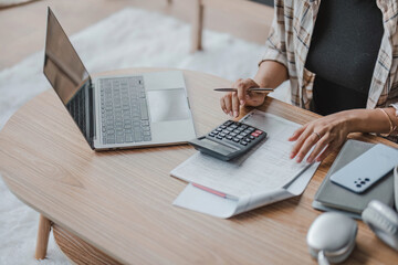 Close-up image of a woman using calculator, calculating money, managing household expenses and taxes in a living room. - obrazy, fototapety, plakaty