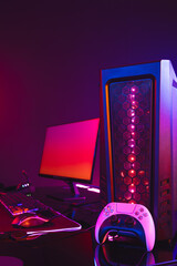 Vertical image of computer with video game accessories with copy space on neon background