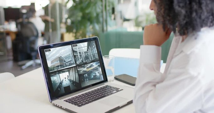 Biracial female security officer watching cctv camera views on laptop in office, slow motion