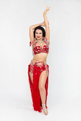 A brunette girl a red dance costume performs oriental dances, a gray background.