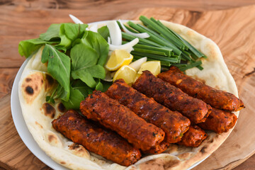 Spicy Chicken kabab meat seekh kebab with bahraini bread tandoori nan, lime and salad served in dish isolated on wooden table top view middle eastern grills food