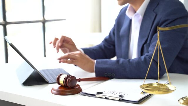 Justice and law concept.Male judge in a courtroom the gavel, working with digital tablet computer on wood table in sun light.