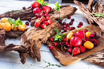 Fresh berries and fruits on a old-fashioned wooden plate on rotten stump. Countryside.