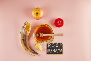 Rosh hashanah lettering - jewish new year holiday concept. Bowl in the shape of an apple with honey, apples, pomegranates, shofar on pink background