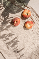 Peaches on beutral beige linen tablecloth background with floral sunlight shadows