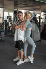 Obraz na płótnie Canvas Beautiful happy fitness couple beautiful slim blondie woman and strong muscular man in sportswear with sneakers stand together in the sport gym