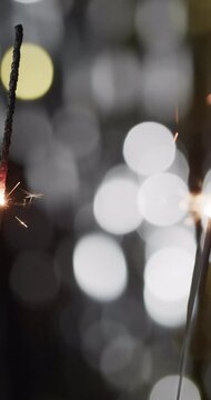 Vertical video of lit sparklers and copy space with bokeh on black background