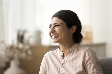 Cheerful beautiful Indian woman looking away with toothy smile, dreaming, thinking, enjoying weekend, break, comfort at cozy home, laughing, showing healthy white teeth - obrazy, fototapety, plakaty