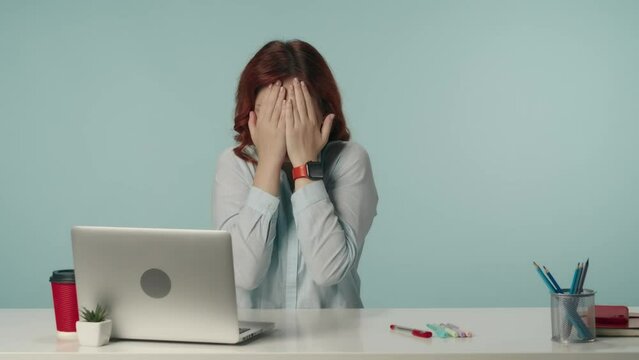 Medium isolated video of a business woman sitting at the desk with laptop and working supplies covering her face in fear and peeping through her fingers.