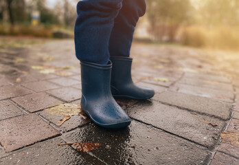Close-up of a child in rubber boots on wet pavement after rain