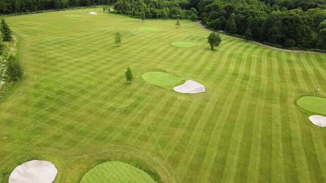 Golf course with its components teeing ground, rough, out of bounds, sand bunker, fairway, putting green, flagstick and hole with a green lawn and several players during the game