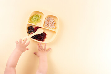 Children's silicone plate with food, the baby's hands reach for dinner. Feeding on a yellow...