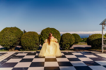 Woman yellow dress chess. A beautiful woman in a long puffy yellow dress poses on a chessboard in...