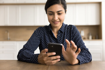 Happy young Indian business woman using mobile phone at home for work communication, sitting at...