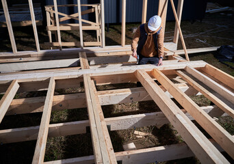 Man worker building wooden frame house on pile foundation. Carpenter hammering nail into wooden plank, using hammer. Carpentry concept.