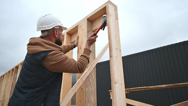 Man worker building wooden frame house. Carpenter hammering nail into wooden joist, using hammer. Carpentry concept.