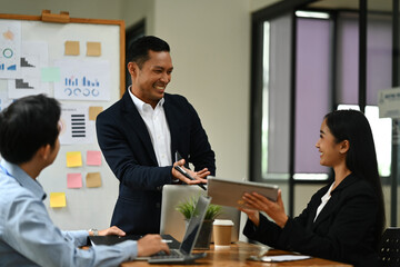 Asian male business team leader discussing project planning and advising on financial data report with his colleagues.
