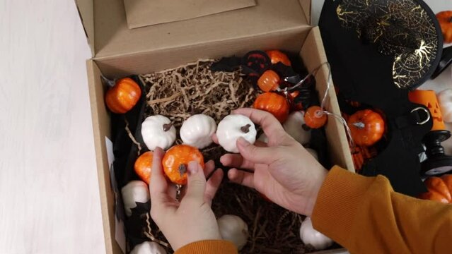 female hands collect halloween decorations in a box, stack pumpkins, packing gifts for halloween