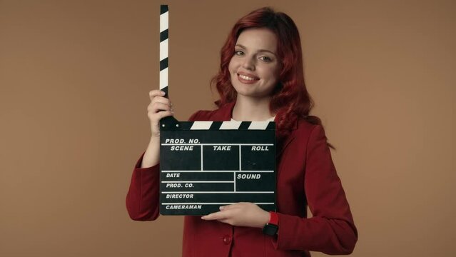 Medium isolated video satisfied, happy and relaxed young woman holding a movie clicker, slate, clapperboard in front of herself, then opening it.