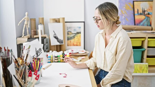 Young blonde woman artist drawing on paper smiling at art studio