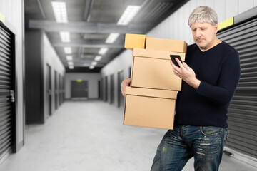 Man near storage room. Businessman with boxes. Guy rents storage room. Man with telephone in warehouse building. Male standing near closed storage room. Corridor with gates in warehouse units