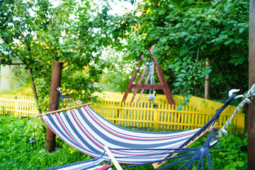Fototapeta na wymiar Striped hammock on poles between trees in a garden or park. 