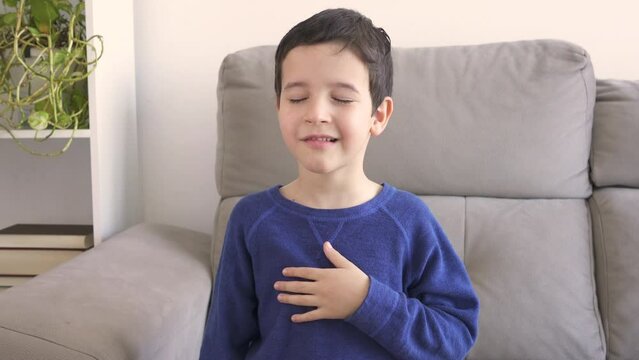Sneezing boy suffering from flu or allergy symptoms sitting on a sofa at home in winter