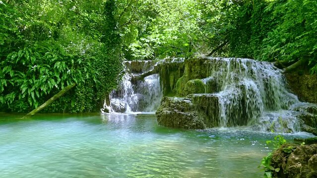 Waterfall with emerald stream in green forest at beautiful sunlight.