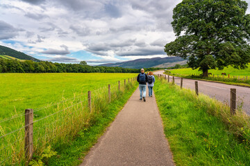 Obraz premium People walking along a roadside path in the highlands of Scotland, UK.