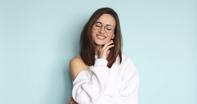 Portrait of flirty young caucasian woman looking at camera with seductive facial expression. Slim beautiful lady in eyeglasses posing on blue background smiling. Sensual woman touch her face.