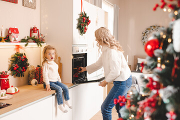 Young mother bake christmas cookies in decorated kitchen at home together. Motherhood. Winter...