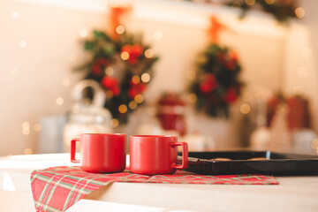 Two red christmas cups with biscuits on kitchen table over xmas background lights close up. Winter holiday season.