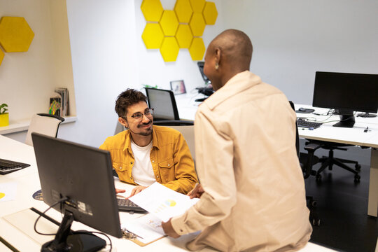 Cheerful Diverse Colleagues Talking In Office During Working At Table With Desktop