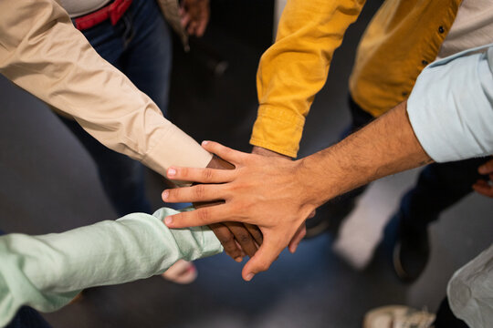 Unrecognizable team members standing together and stacking hands in light