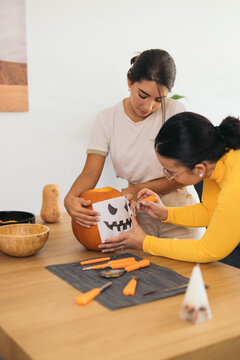 Young ethnic women standing at table with Halloween paper print on pumpkin