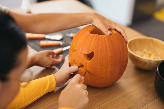 Unrecognizable women sitting at table and preparing Halloween pumpkin