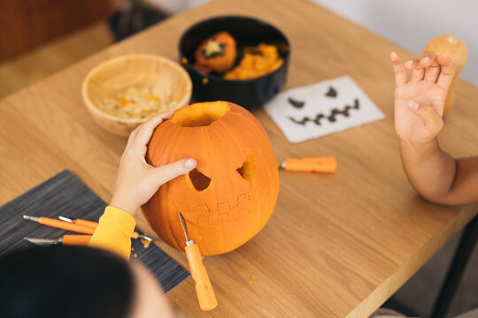 Unrecognizable women sitting at table and preparing Halloween pumpkin
