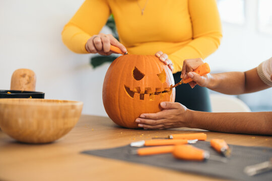 Unrecognizable women near table and carving Halloween pumpkin in daylight
