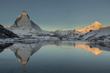 Snowy mountains in winter day near lake under dark sky at sunrise