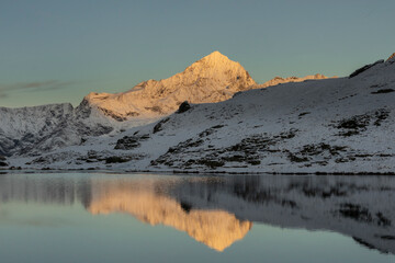 Snowy mountains in winter day near lake under dark sky at sunrise