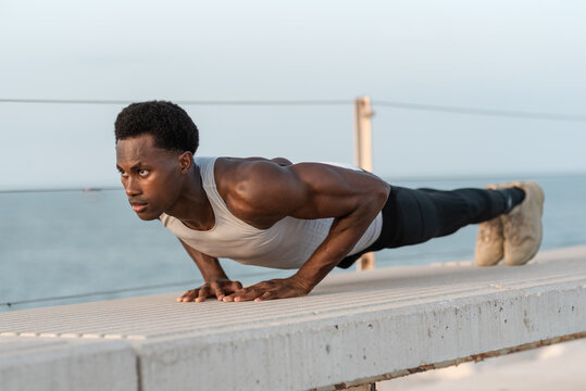 Strong black man doing plank exercise on parapet
